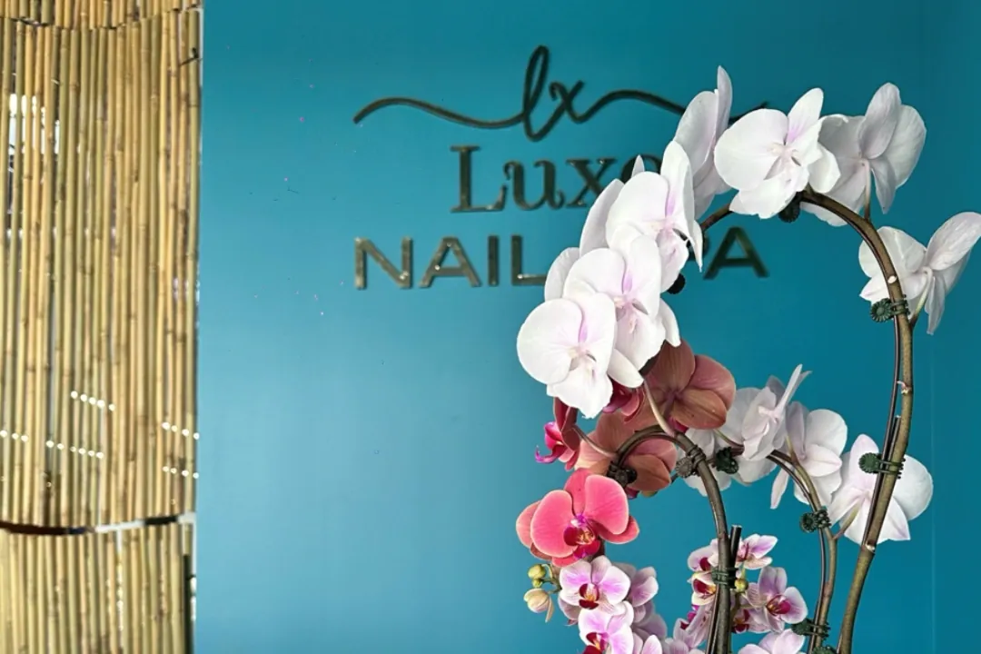 Luxo Nail Spa sign on a teal wall behind pink and white orchids